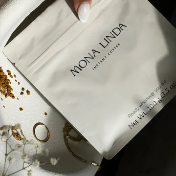 Mona Linda instant coffee pouch on white surface with decorative jewelry pieces around it.